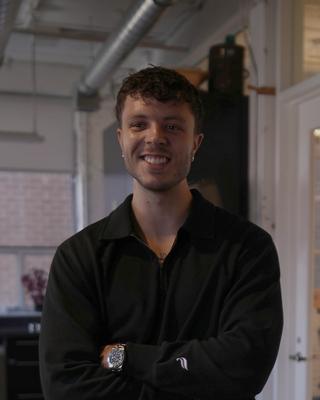 Matt smiling in the office with his arms folded, in a black shirt.