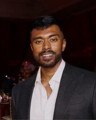 Nafis smiling at an evening event, in a dark suit jacket and an open white shirt.